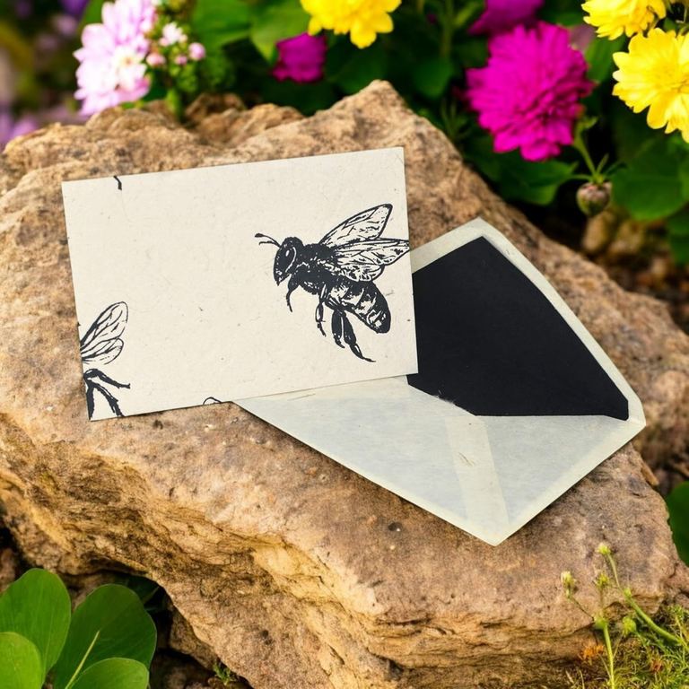A Bees card with its black-lined envelope on a rock among bright flowers