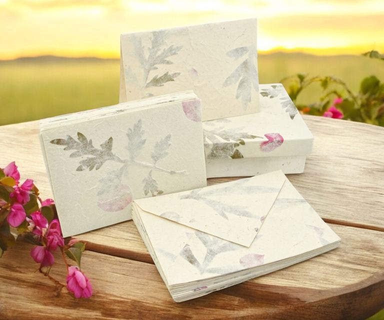 Forest Wanderer cards, envelopes and box on a round wooden table at sunset, pink flowers beside them
