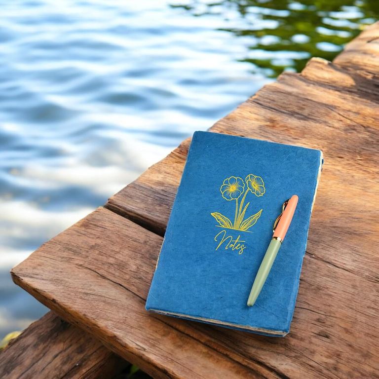 The Indigo Heritage Deluxe Companion notebook with a pen on a wooden dock above the water
