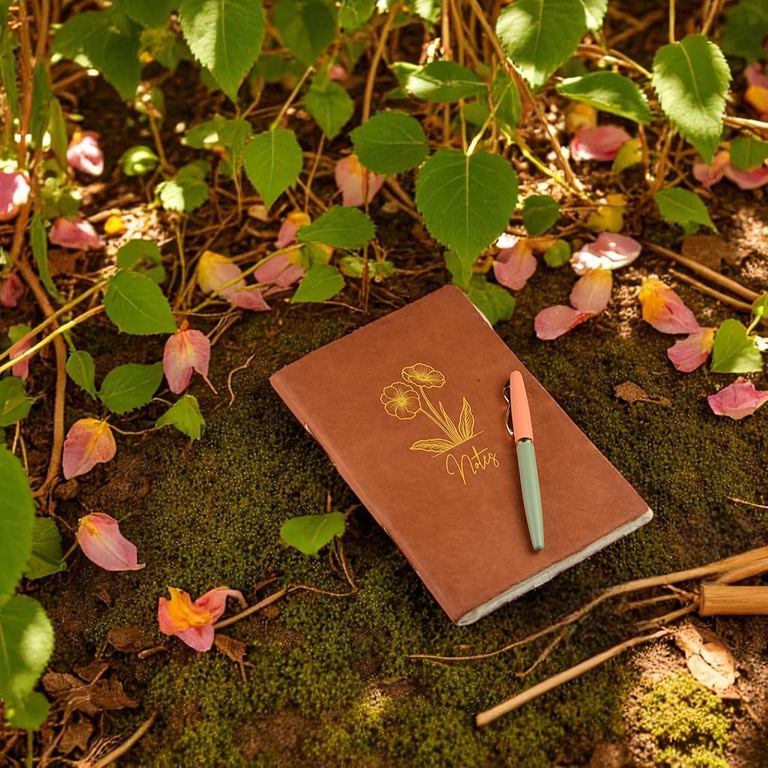 The Terra Cotta Heritage Deluxe Companion notebook with a pen on moss and fallen leaves