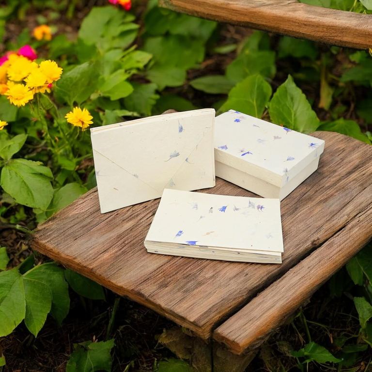 Cornflower lokta greeting cards, envelopes and their box on a weathered board among garden flowers