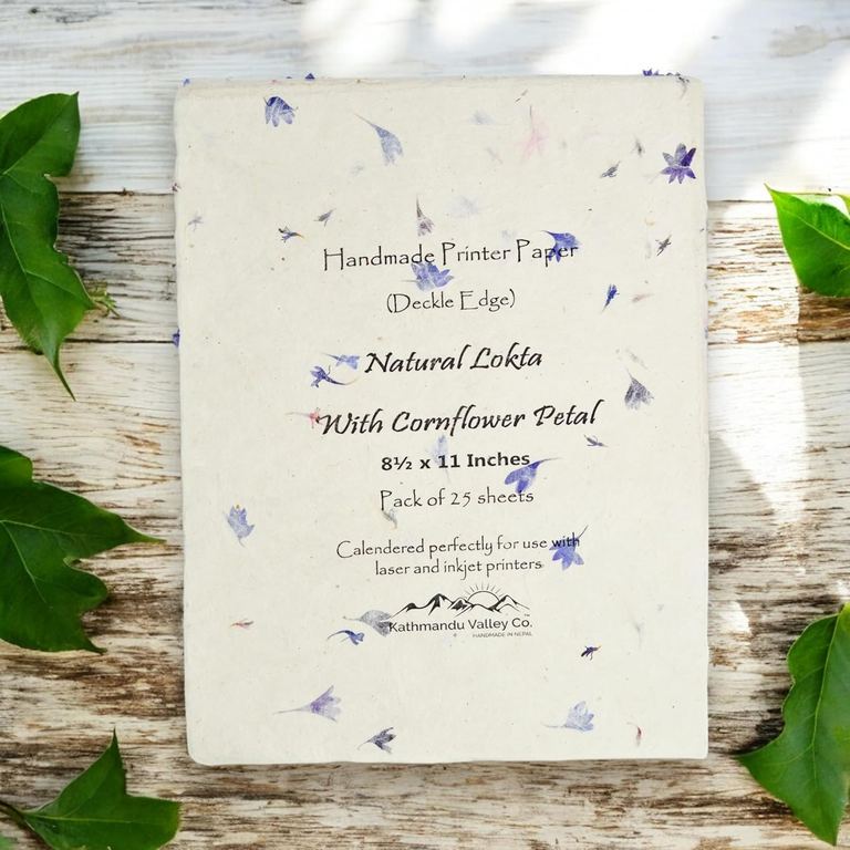 A packet of handmade cornflower petal lokta printer paper on a whitewashed board with ivy leaves