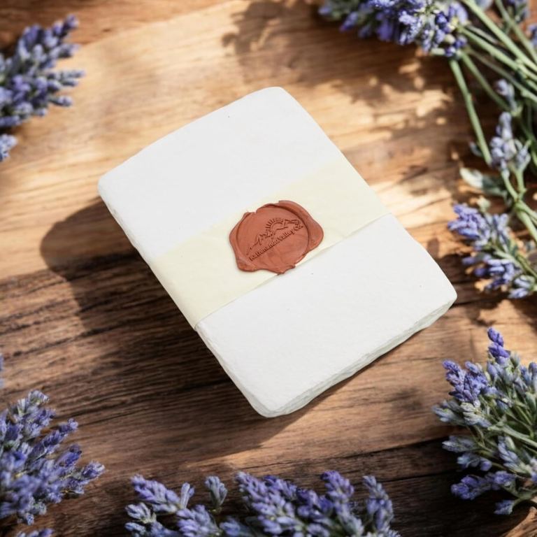 A banded pack of white 5×7 cotton card stock with a wax seal on weathered wood, lavender all around