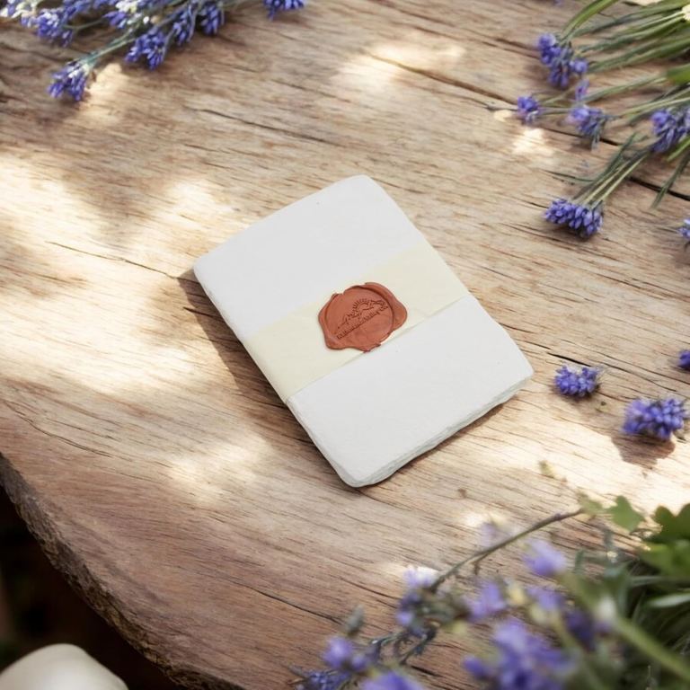 A small pack of white 5×7 cotton card stock in dappled sunlight on an old wooden table