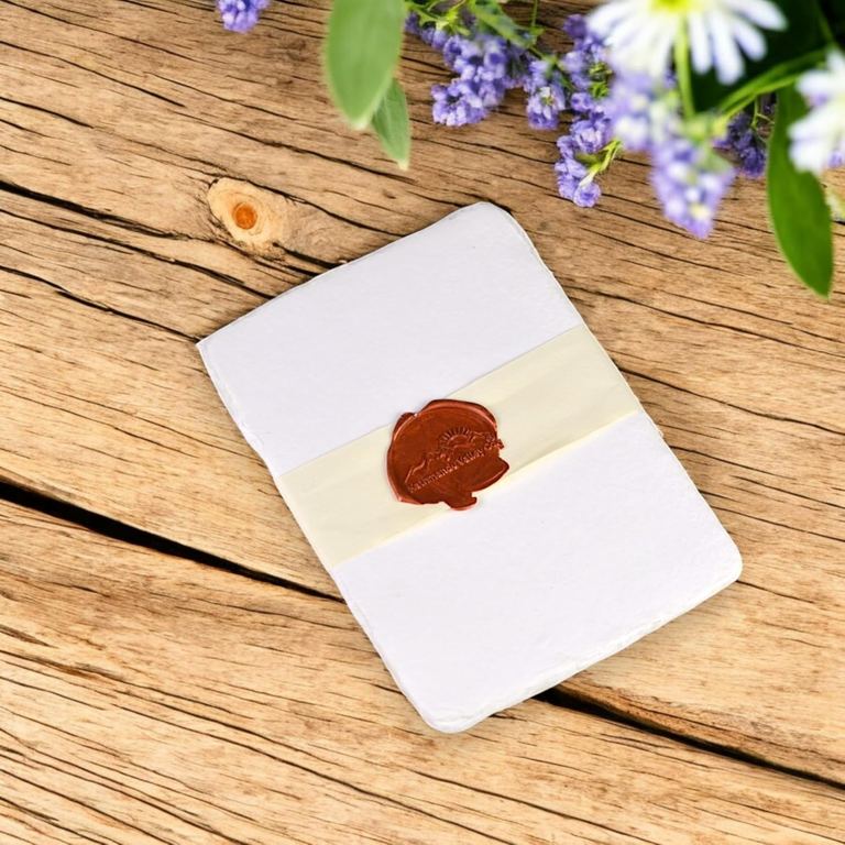 A banded pack of white 5×7 cotton card stock with a wax seal on rustic wood, lavender and daisies at the top