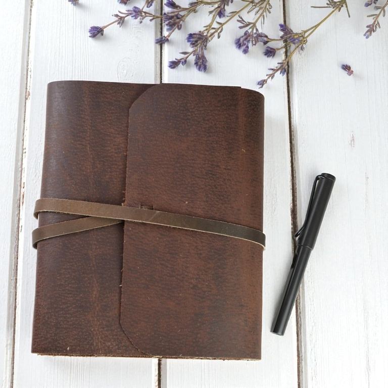 The large Everest Explorer journal closed, its leather strap tied, on white boards with a pen