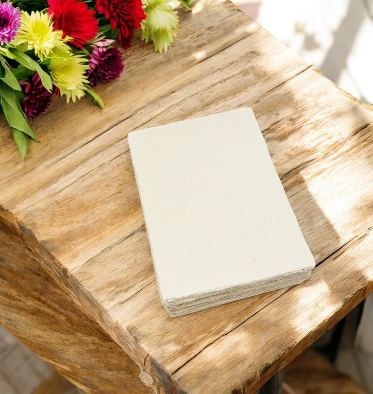 A stack of Deluxe 5×7 card stock on a sunlit wooden table with flowers