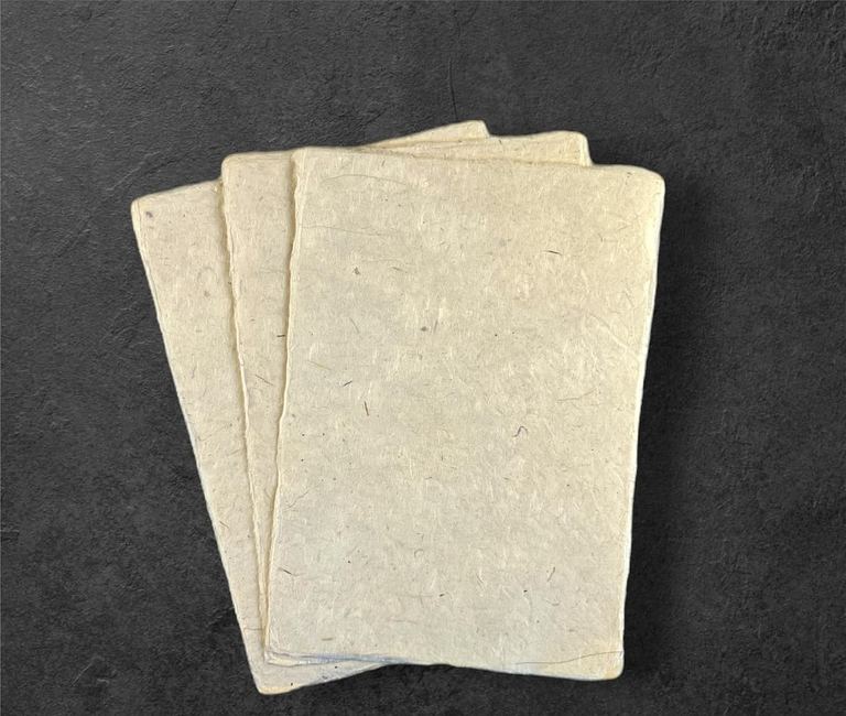 Three sheets of natural lokta card stock on dark slate, flecks of bark showing in the paper