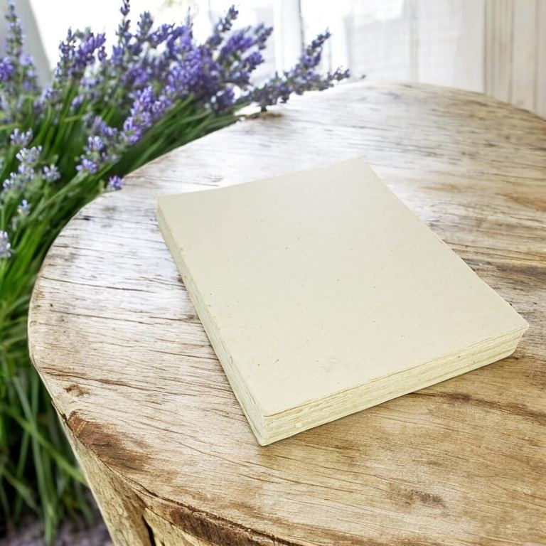A stack of 8.5 × 11 Deluxe lokta card stock on a round weathered table beside lavender