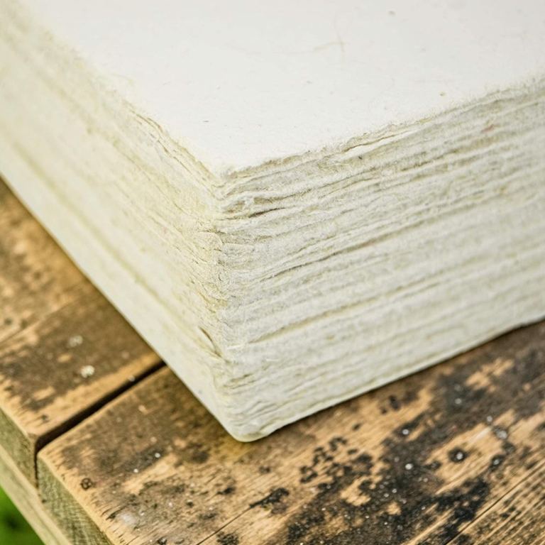 The deckled edges of a 100-sheet stack of traditional lokta card stock on dark weathered wood