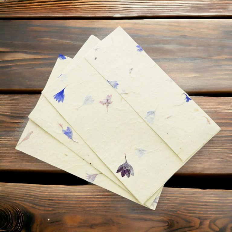 Three cornflower 4×6 lokta envelopes fanned out on dark wooden boards