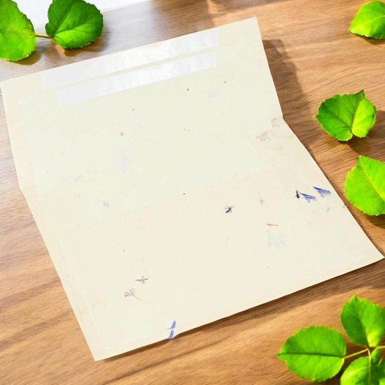 A cornflower lokta envelope with its flap open, showing the self-seal strip, on a sunlit wooden table