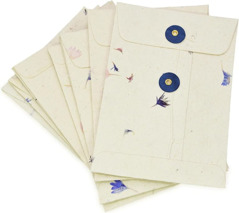 Cornflower lokta pocket envelopes fanned out, petals scattered through the paper