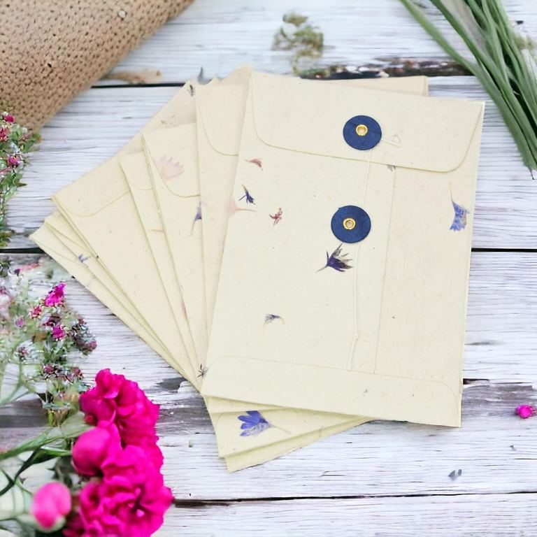 Cornflower lokta pocket envelopes with blue buttons fanned on whitewashed boards beside pink flowers