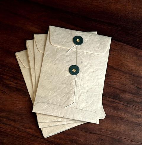 Natural lokta pocket envelopes with sage green buttons on a dark wooden table