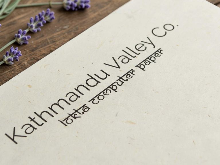 A sheet of Kathmandu Valley Co. natural lokta computer paper on a dark wooden table beside sprigs of lavender