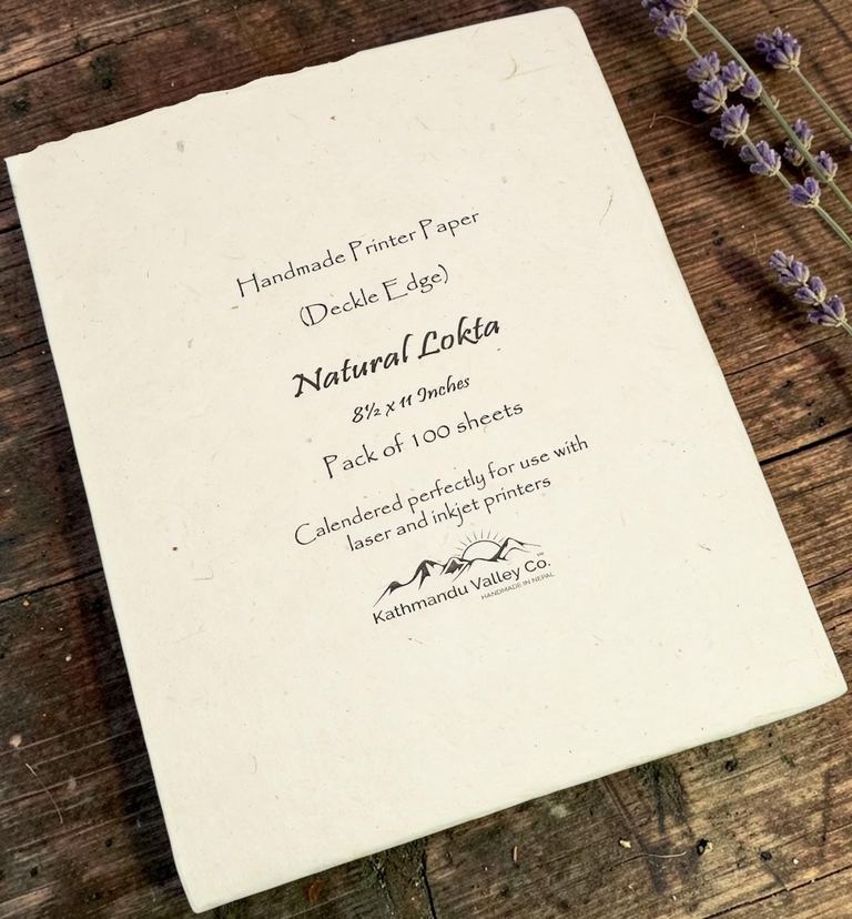 A 100-sheet packet of natural lokta printer paper with a deckle edge on a dark wooden table beside sprigs of lavender