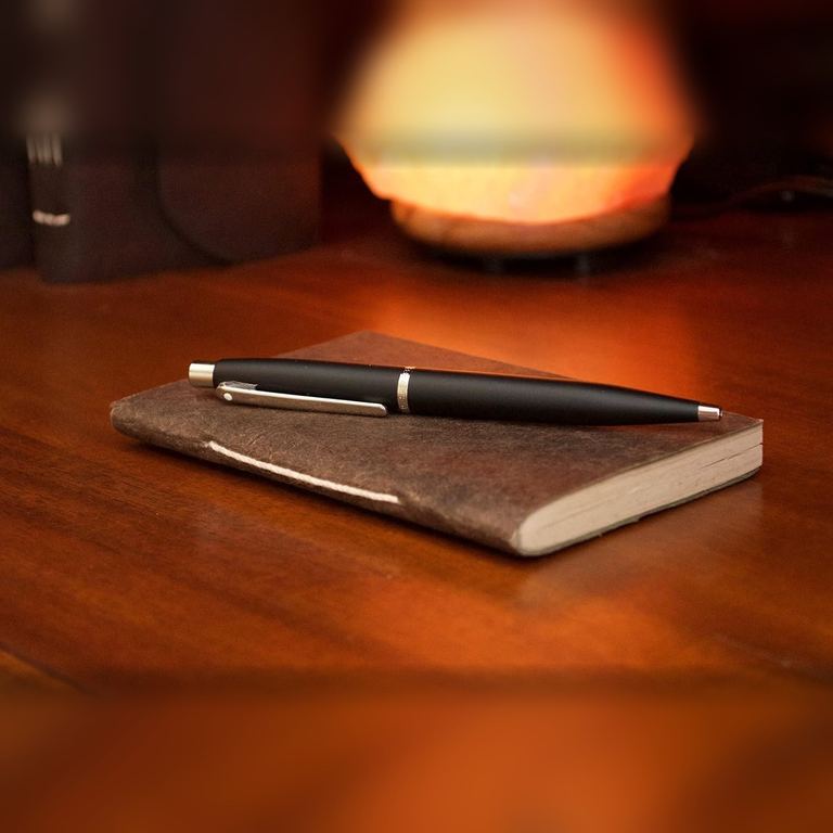 The Pocket Dark Walnut Nepali Companion notebook with a pen on a polished wooden desk