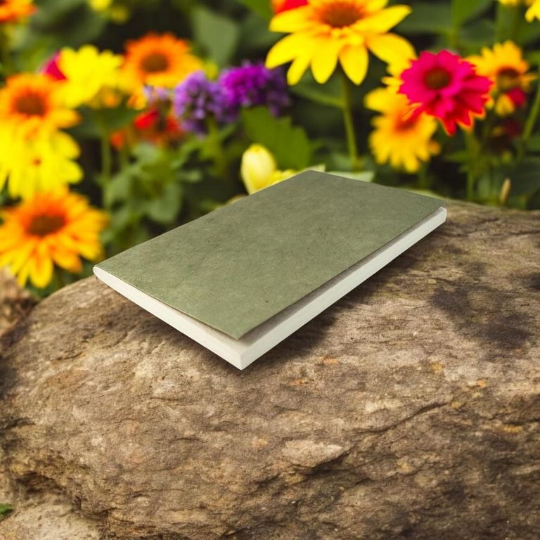The Sage Nepali Companion notebook on a rock in front of yellow and pink flowers