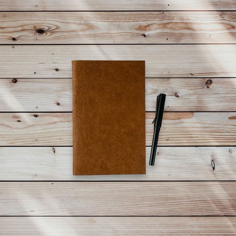 The Terra Cotta Nepali Companion notebook on weathered wooden planks beside a pen