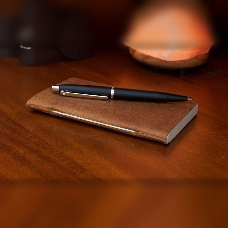 The Pocket Terra Cotta Nepali Companion notebook with a pen on a polished wooden desk