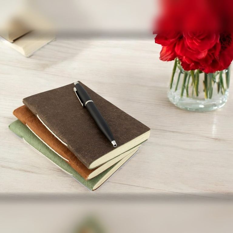 Pocket Dark Walnut, Terra Cotta and Sage Nepali Companion notebooks stacked with a pen, red roses behind
