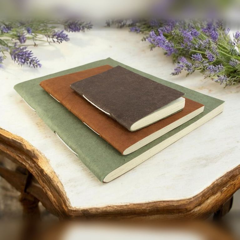 Large Sage, Medium Terra Cotta and Pocket Dark Walnut Nepali Companion notebooks stacked on a table with lavender