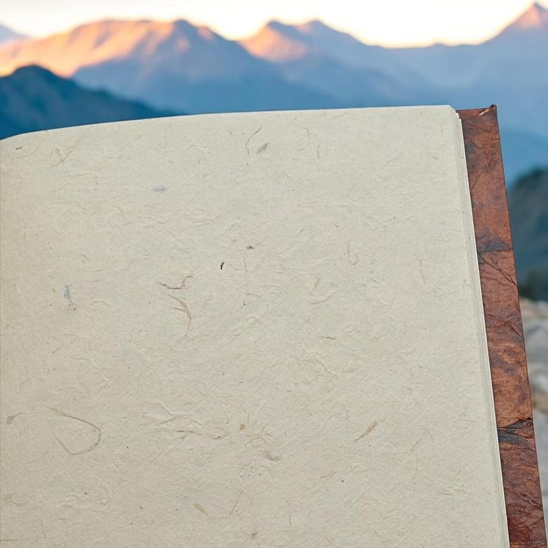 A Nepali Eco journal open to a blank page of textured lokta, mountains behind