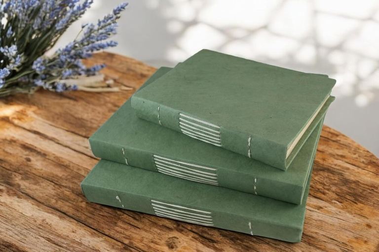 Sage Nepali Keeper journals in three sizes stacked on a wooden table with lavender