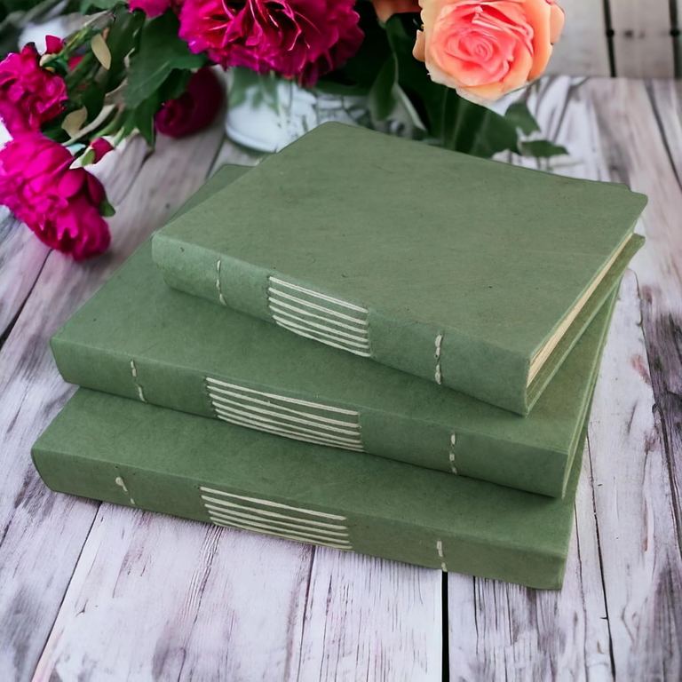 Three Sage Nepali Keeper journals stacked on a whitewashed table beside roses