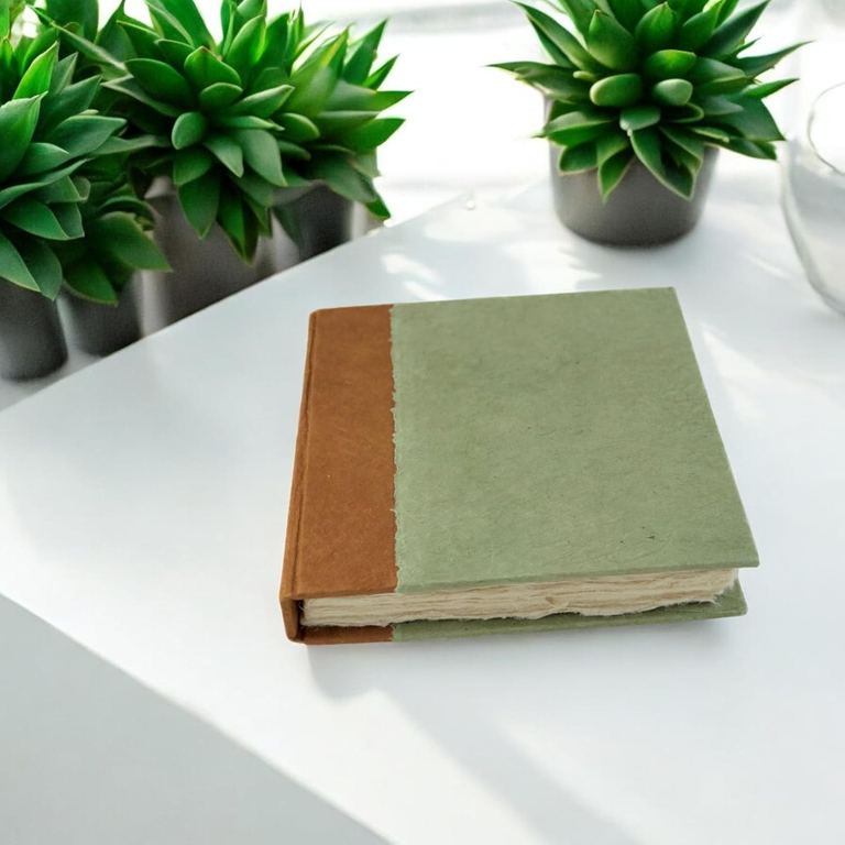 The 6 × 6 Sage Nepali Namaste journal on a white table beside potted succulents