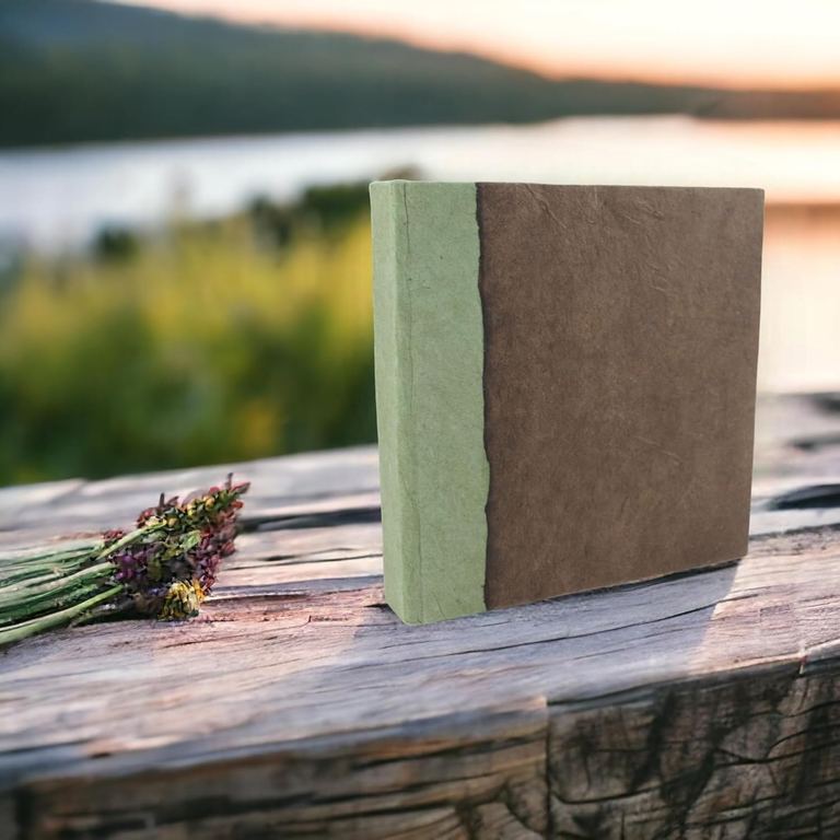 The 6 × 6 Dark Walnut Nepali Namaste journal on a weathered log by a lake at sunset, lavender beside it