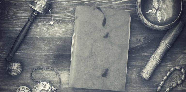 A leather Nepali Yeti Tracker journal on a wooden table with a prayer wheel, a singing bowl and prayer beads, in black and white