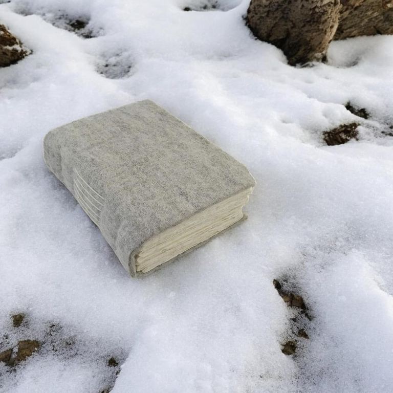 The wool felt Nepali Yeti Tracker journal lying in the snow among rocks