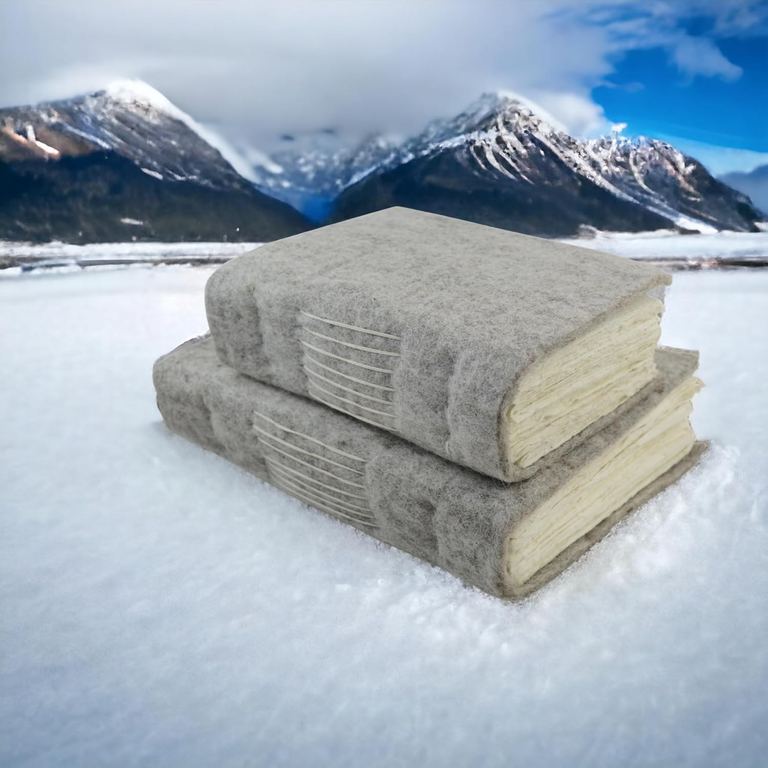 The 5 × 8 and 8 × 10 wool felt Nepali Yeti Tracker journals stacked on snow, snowy peaks behind